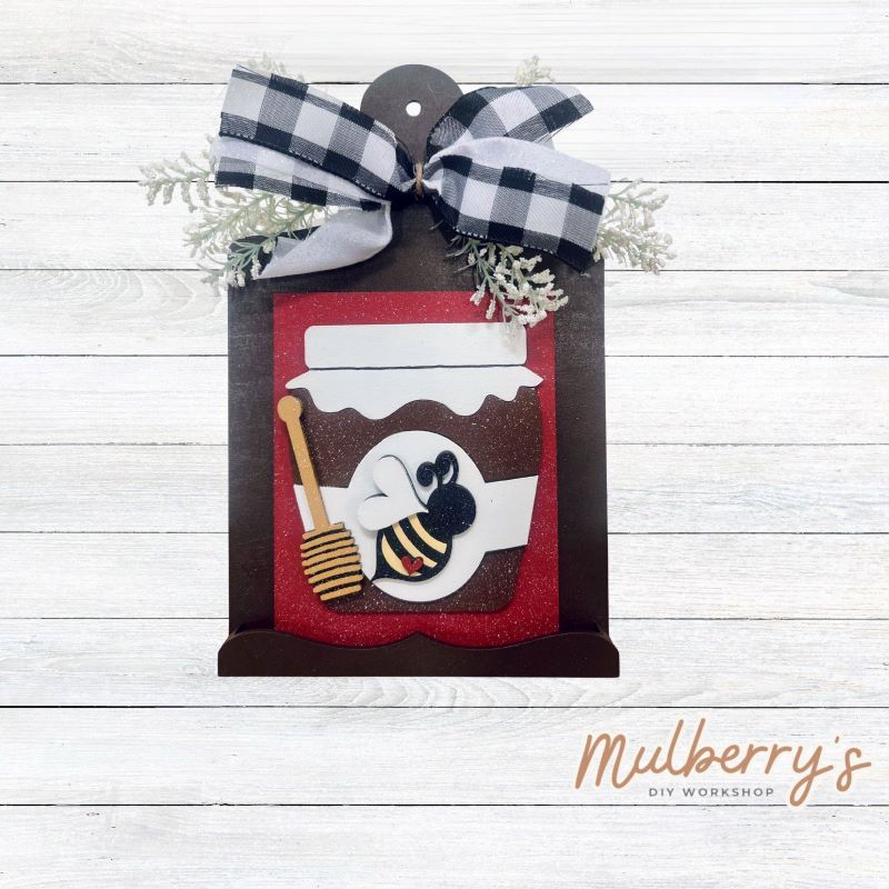 Our Interchangeable Mini Breadboard measures roughly 6.5" wide & 10.5" tall.
This project can easily be changed out for holidays, seasons and other themes. Because the breadboard leans back with the use of an easel, no magnets or adhesive hook and loop is needed.
The set includes the mini breadboard and honey jar insert.