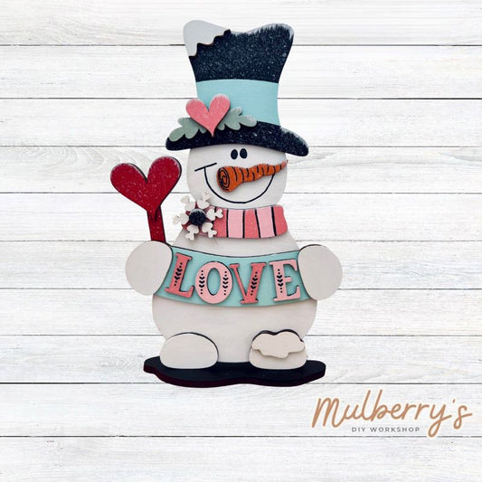 Love is in the air with this adorable project! This cute little snowman stand-up shelf sitter measures at approximately 10.5" tall. Includes stand.